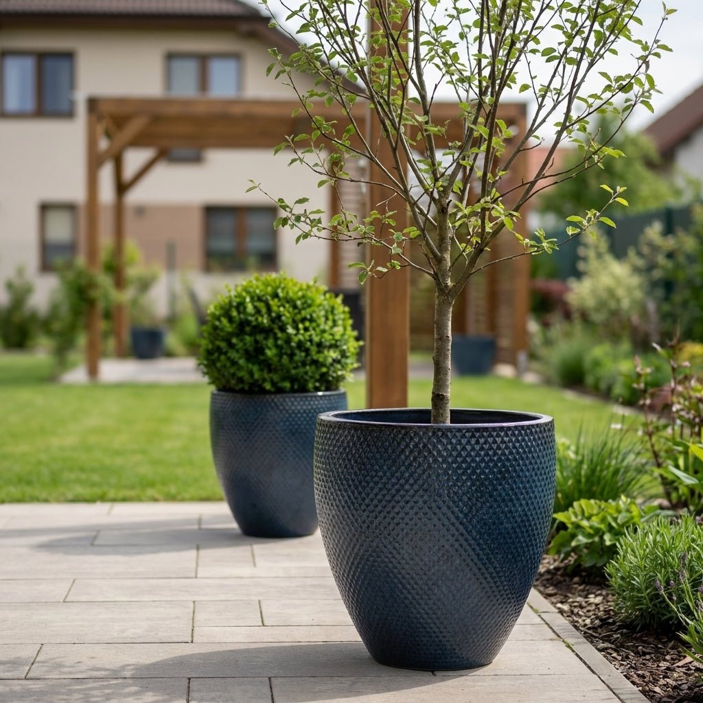 Detailní pohled na keramický květináč Signac - Antická modrá o výšce 52 cm s okrasným keřem na moderní prosluněné terase.