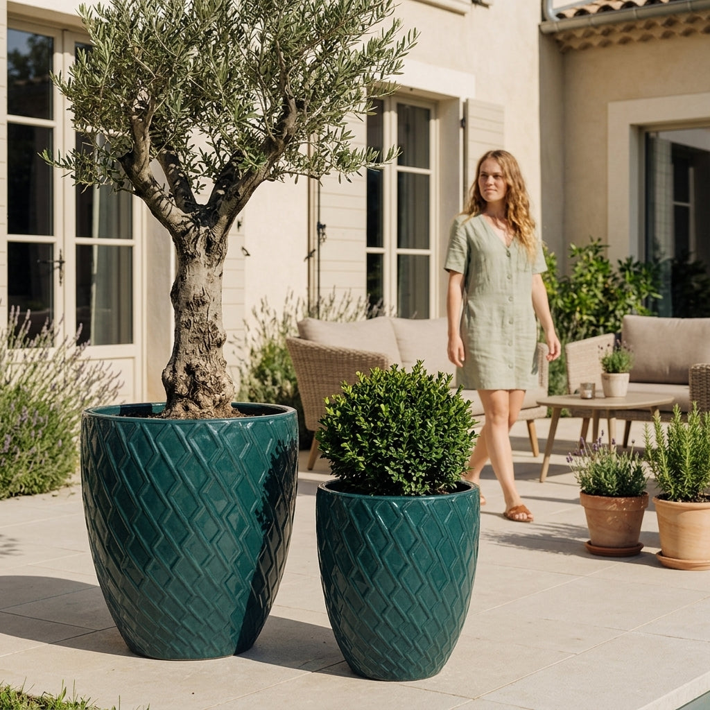 Detailní pohled na Keramický květináč Zeus - Petrolejová modrá s olivovníkem. Vyniká lesklá glazura a okrasný reliéf na prosluněné kamenné terase.
