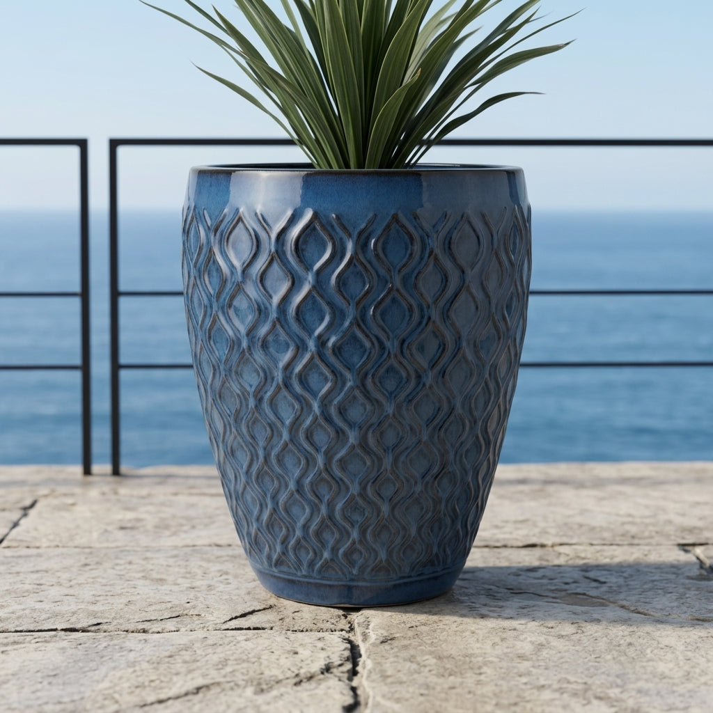 Detailní pohled na Keramický květináč Phenix - Antická modrá s rostlinou Cordyline na kamenné terase s výhledem na oceán.