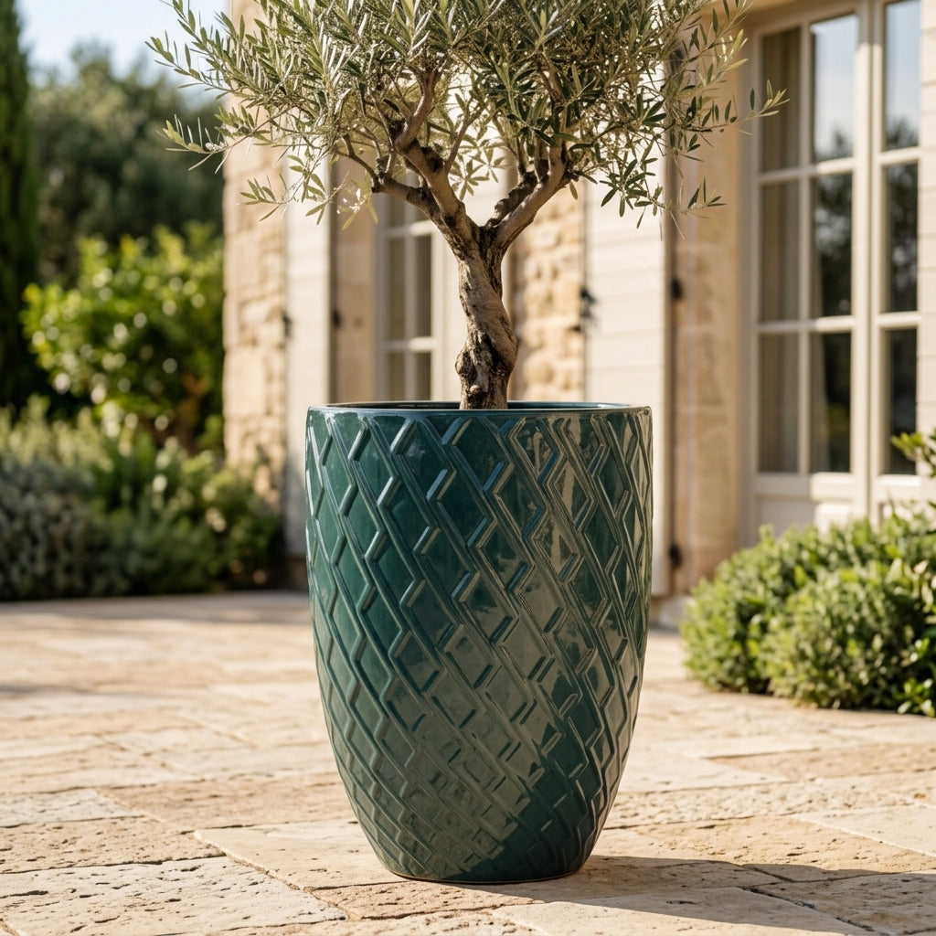 Detailní pohled na Keramický květináč Zeus - Petrolejová modrá s olivovníkem. Vyniká lesklá glazura a okrasný reliéf na prosluněné kamenné terase.