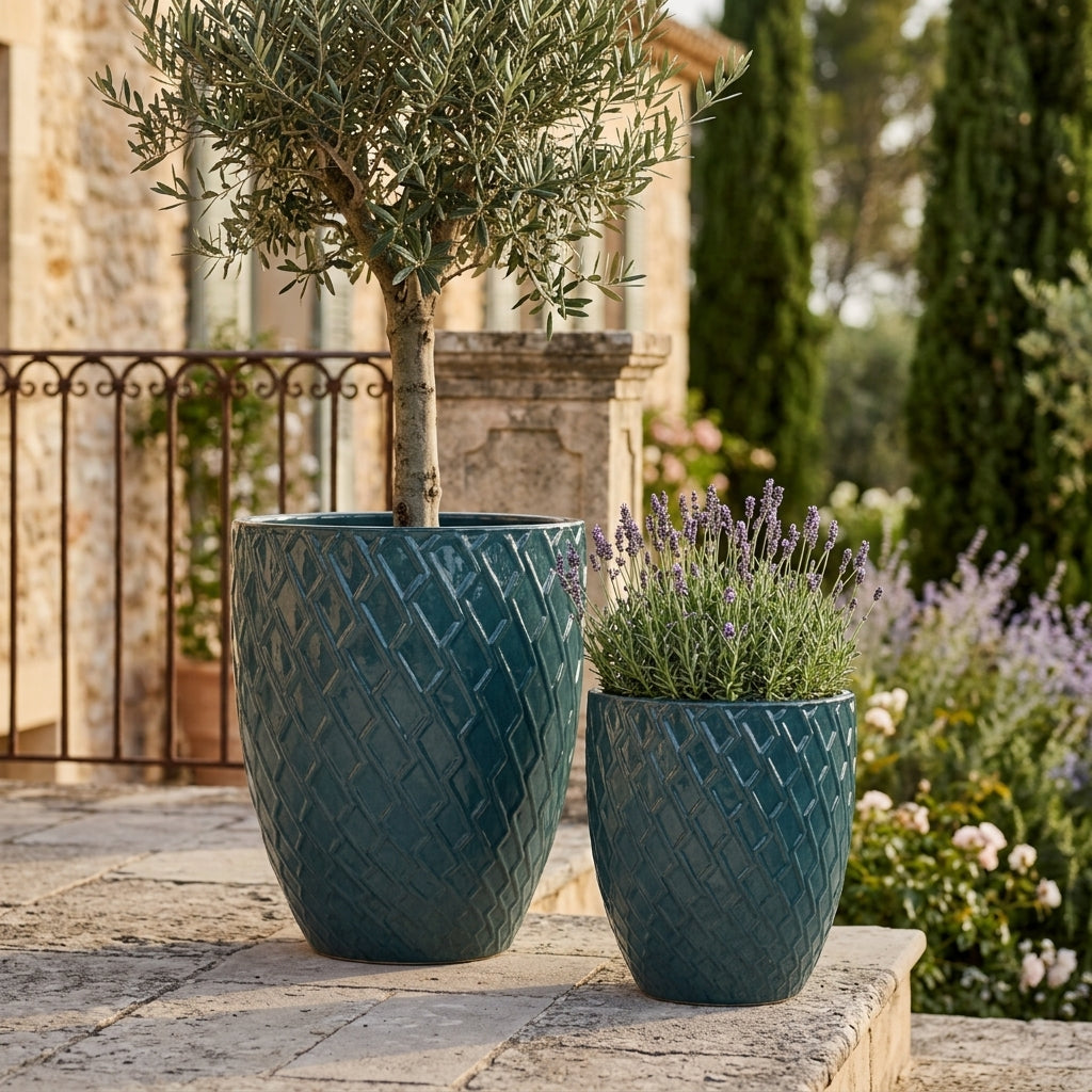 Detailní pohled na Keramický květináč Zeus - Petrolejová modrá s olivovníkem. Vyniká lesklá glazura a okrasný reliéf na prosluněné kamenné terase.