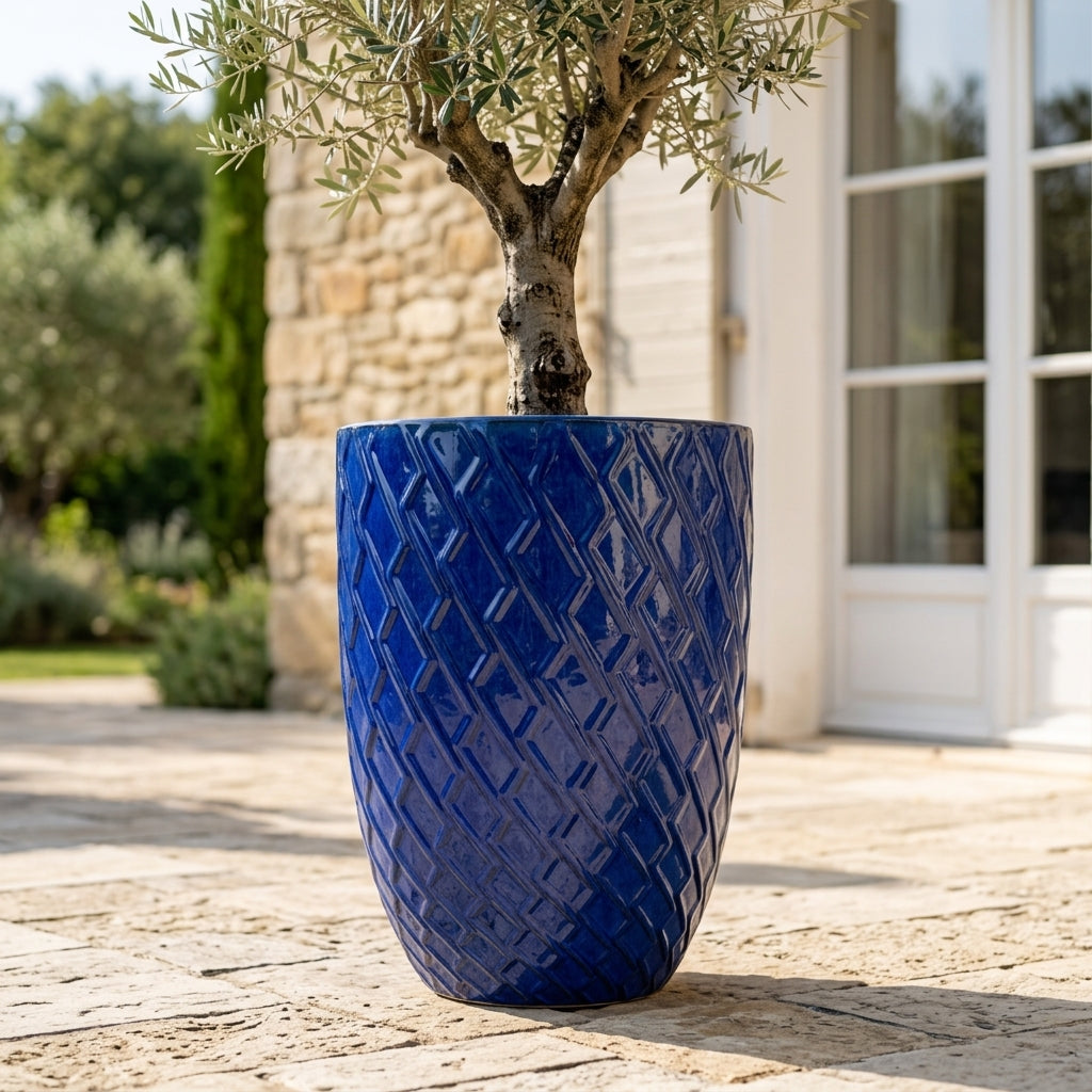 Detail velkého keramického květináče Zeus - Antická modrá s okrasným reliéfem a zasazeným olivovníkem na slunné kamenné terase.